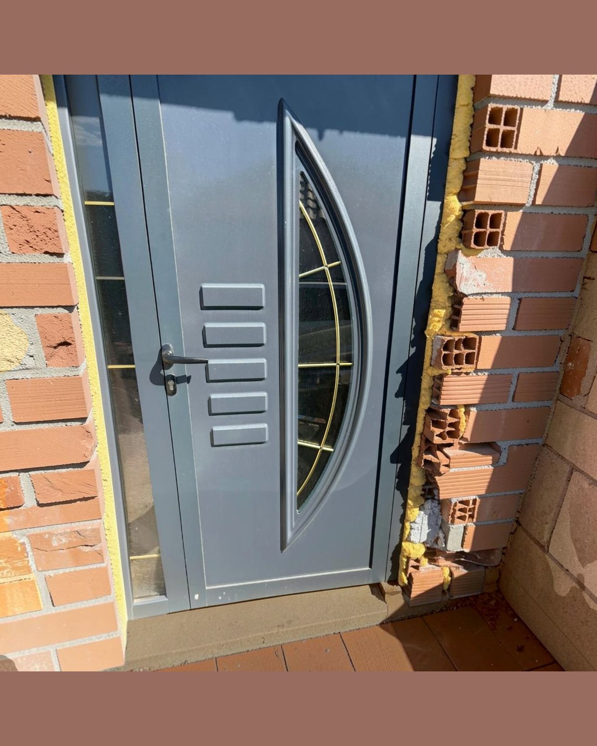 SK14T grey door panel with gold bars and a sidelight, installed on a brick façade